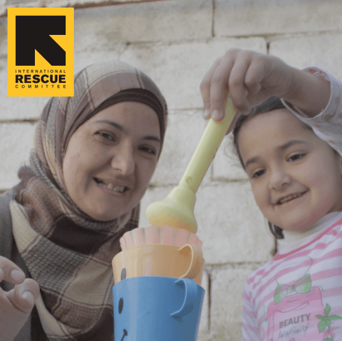 A woman in a hijab plays watches her daughter playing with toys.